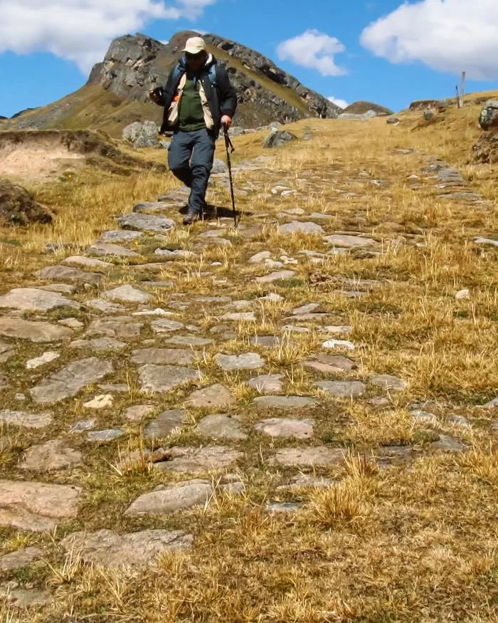 El caminante avanza por el Qhapaq Ñan, un antiguo camino inca que aún conserva su trazo original entre montañas andinas.