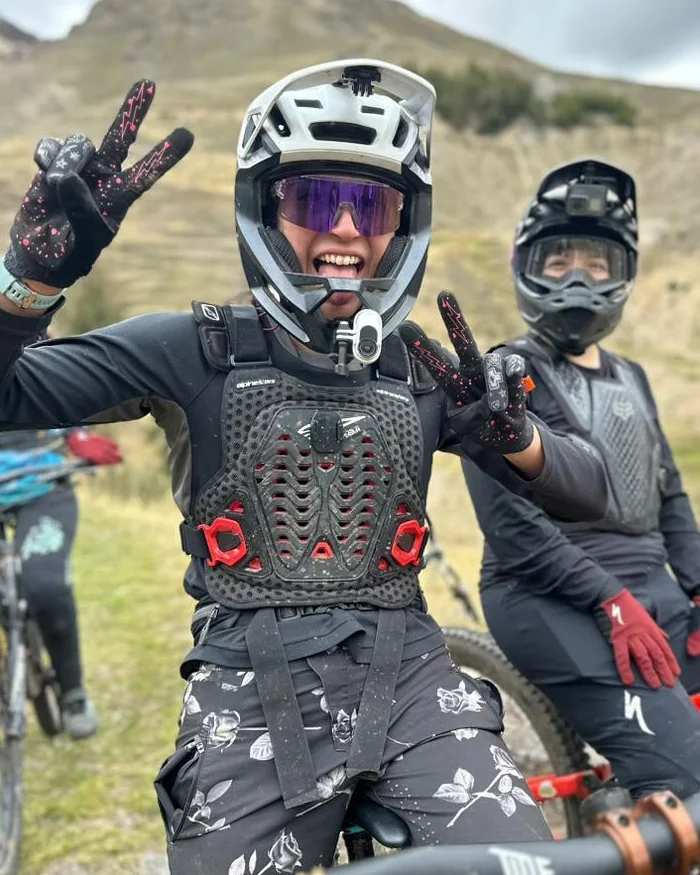 La imagen muestra a dos ciclistas de montaña completamente equipados, disfrutando de una pausa en plena ruta de alta montaña.