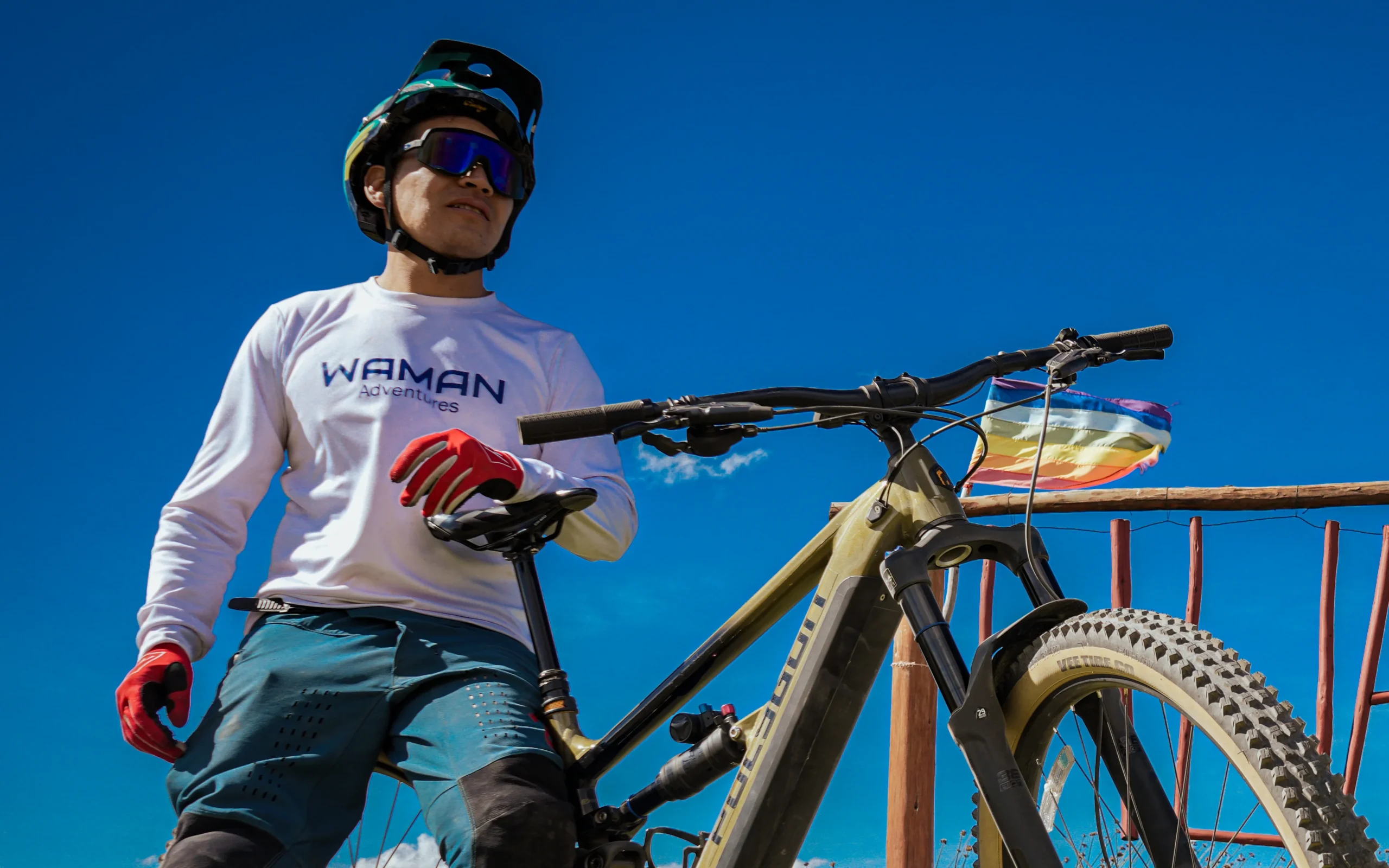 Mountain biker rests beside his bike on a rural viewpoint near Cusco, Peru, looking over Andean hills and open sky.