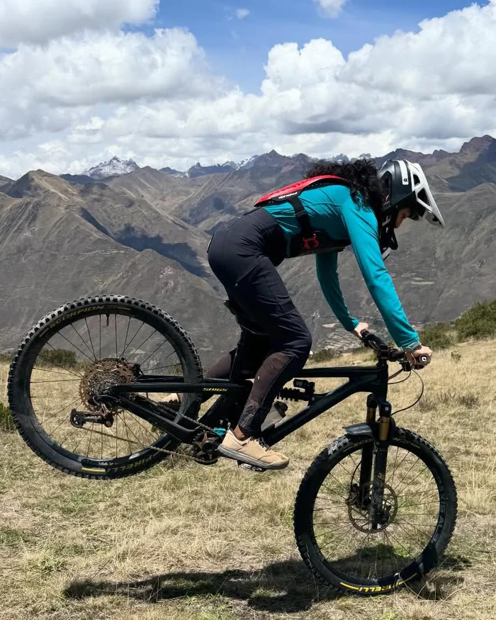 Mountain biker rides a highland trail near Cusco, Peru, holding a technical stance on open terrain with wide panoramic mountain views.