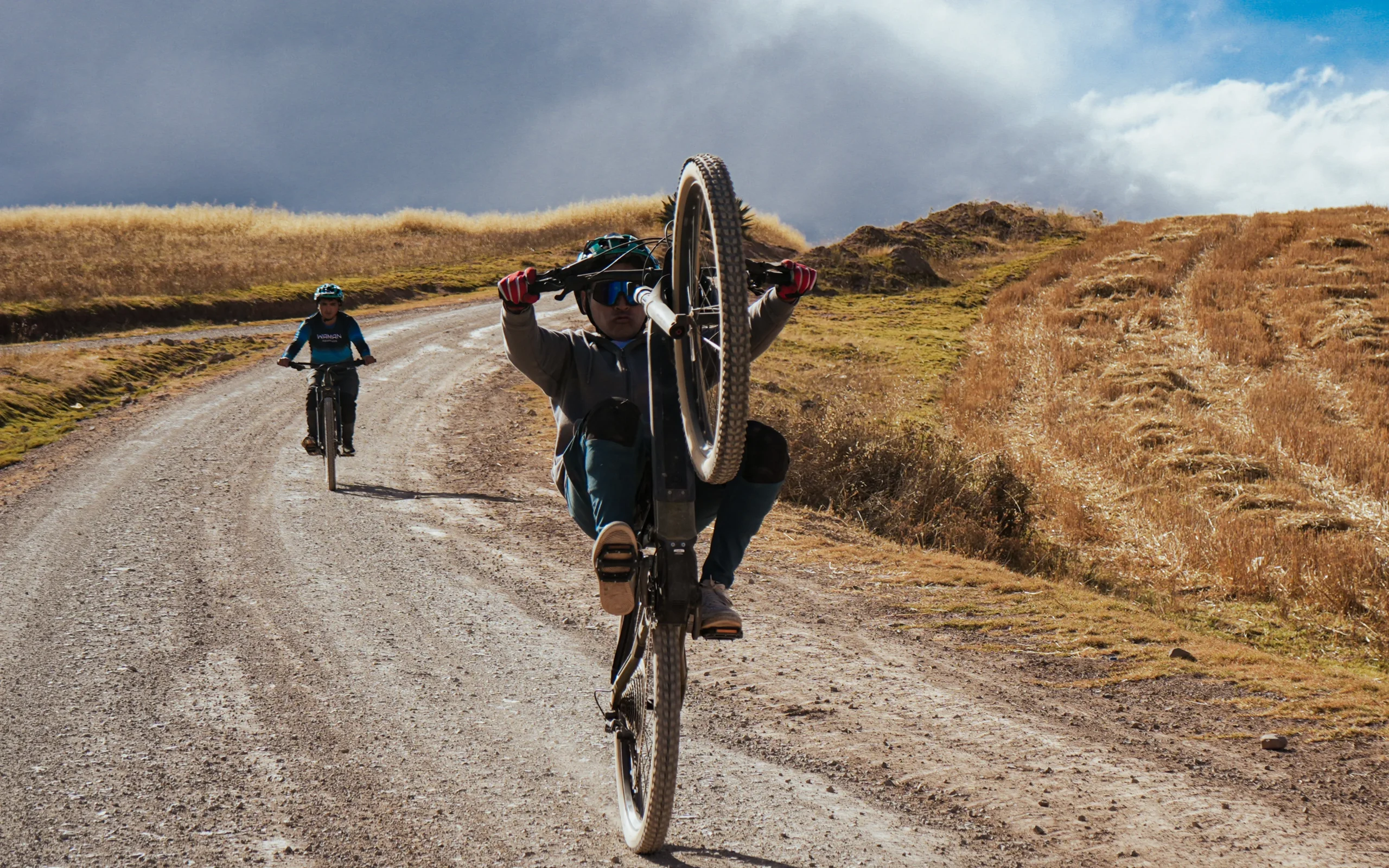 Cyclist rides a winding dirt road through rolling hills in the Sacred Valley near Cusco, Peru, under bright sky.