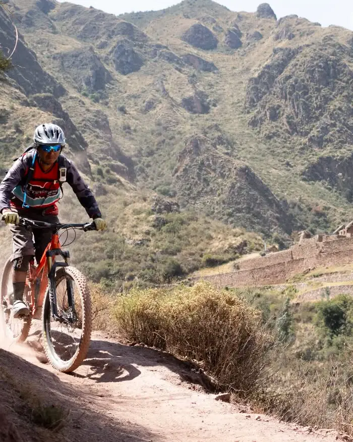 Un ciclista de montaña desciende por un sendero angosto tallado en la ladera, levantando polvo a su paso.