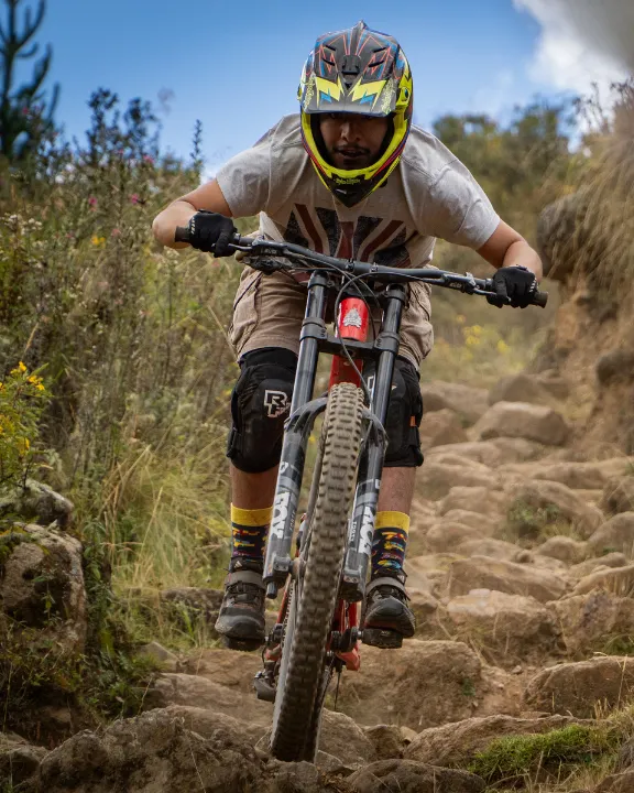 Close up downhill cyclist tackling a stone step section in Lamay, Sacred Valley, Cusco, Peru, wearing full face helmet and gloves on rocky trail.