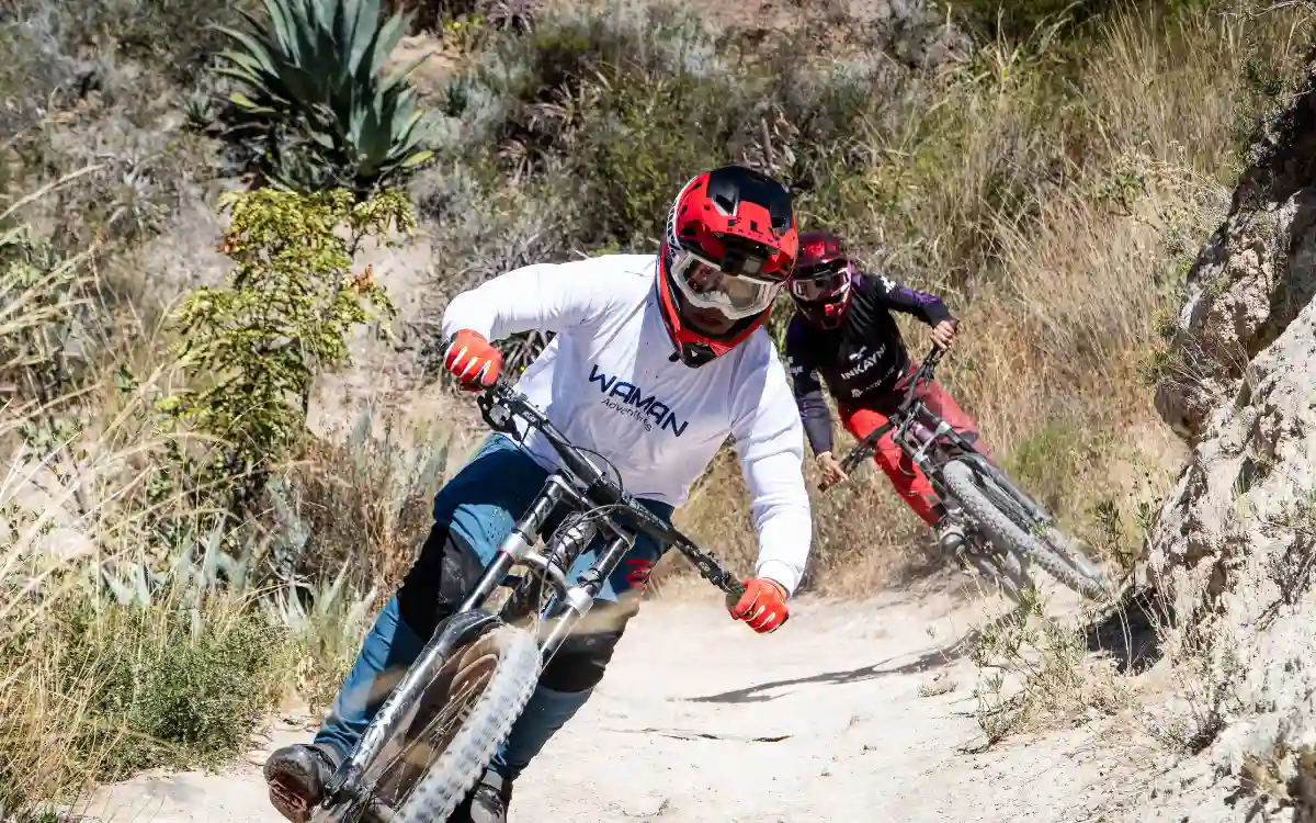 Ciclista trazando una curva cerrada en una línea angosta y polvorienta de Maras, Valle Sagrado, Cusco, Perú, con casco integral.
