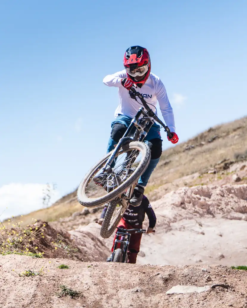 Mountain biker lifting the front wheel on a rocky Maras ridgeline trail in the Sacred Valley near Cusco, Peru, under bright sun.