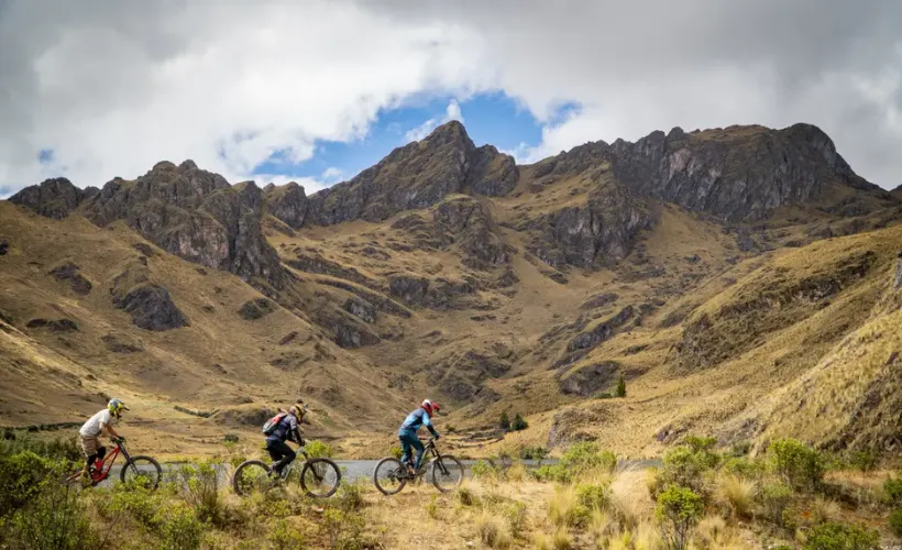 La ruta MTB Huama de altura desde la Laguna Huama hacia Lamay, Valle Sagrado, Cusco, Perú, con montañas al fondo, planicie abierta y cielo despejado.
