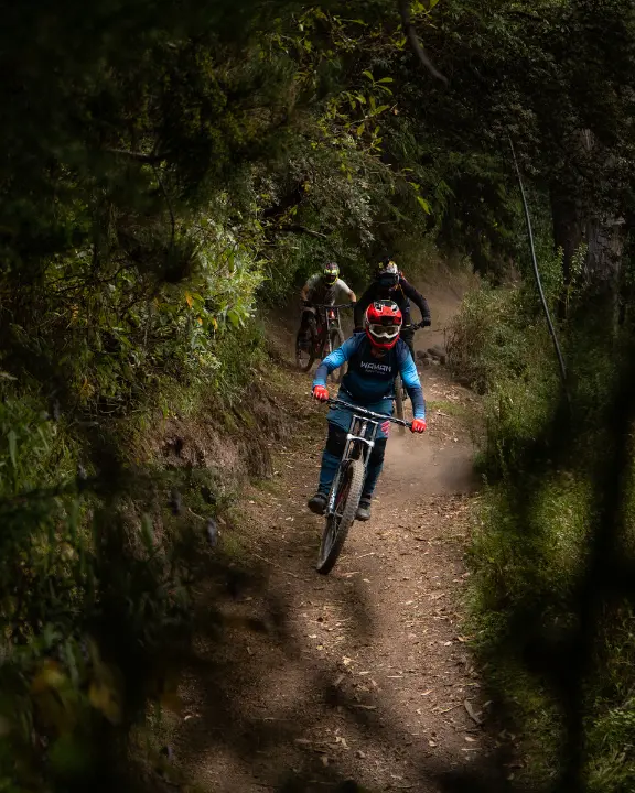 Mountain biker threading a shaded forest singletrack tunnel in Lamay, Sacred Valley near Cusco, Peru, with trees, brush, and narrow dirt trail.