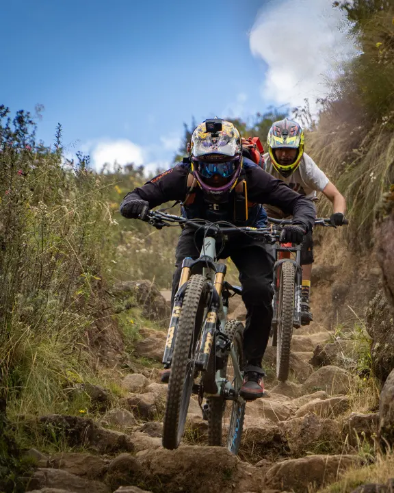 Grupo de riders bajando escalones rocosos en un tramo técnico de Lamay, Valle Sagrado, Cusco, Perú, con cascos integrales y protecciones.