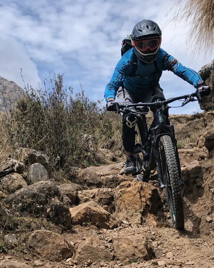 Downhill rider on a rugged mountain track in Cusco, Peru, wearing a full face helmet, working suspension and brakes on loose dirt.