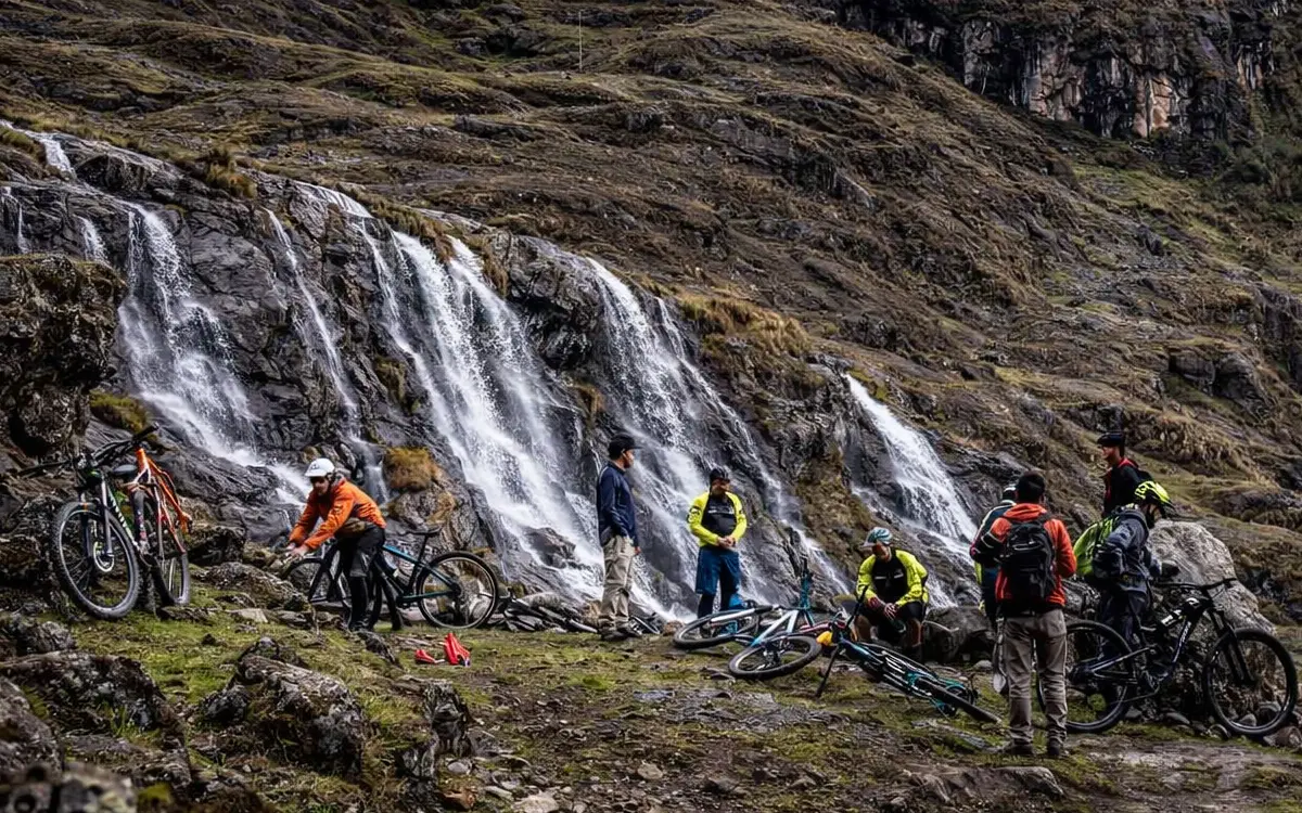 La escena muestra un riding de montaña en un entorno natural abierto, con agua, roca y desniveles pronunciados.