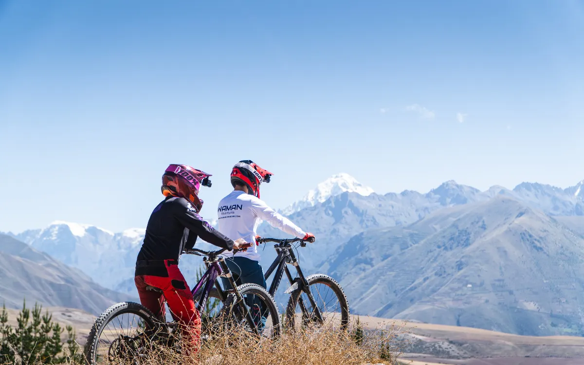Two cyclists pause at a Maras viewpoint in the Sacred Valley near Cusco, Peru, with their bikes and a wide mountain panorama.