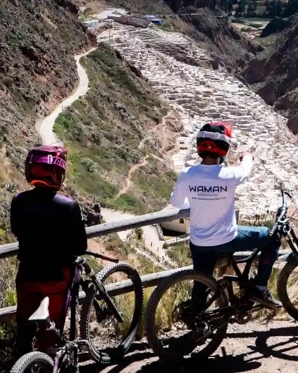 Dos ciclistas descansando en un mirador sobre el cañón del Valle Sagrado desde Maras, Cusco, Perú, con bicicletas junto a una baranda.
