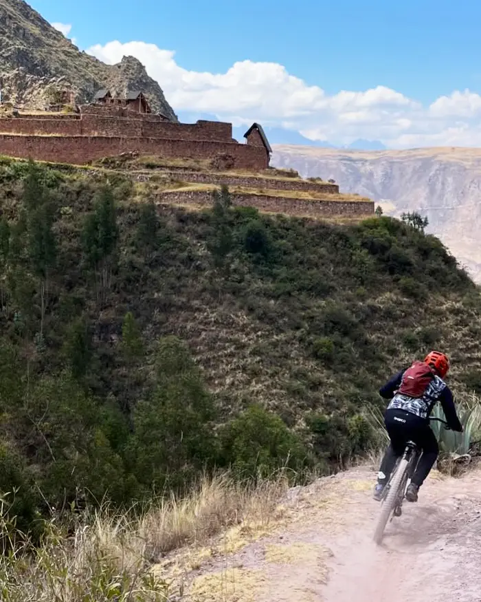 Un ciclista desciende por un sendero angosto y polvoriento en una ladera expuesta sobre un valle profundo.