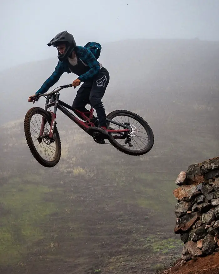 A mountain biker is in midair while jumping from a stone ledge on a high-mountain trail.
