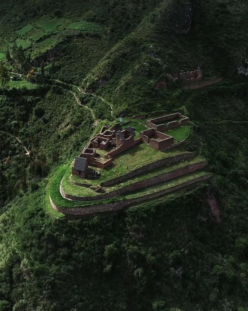 Aerial view of the ancient stone ruins and agricultural terraces of the Complejo Arqueologico de Raqaypata surrounded by steep green mountains in Cusco.