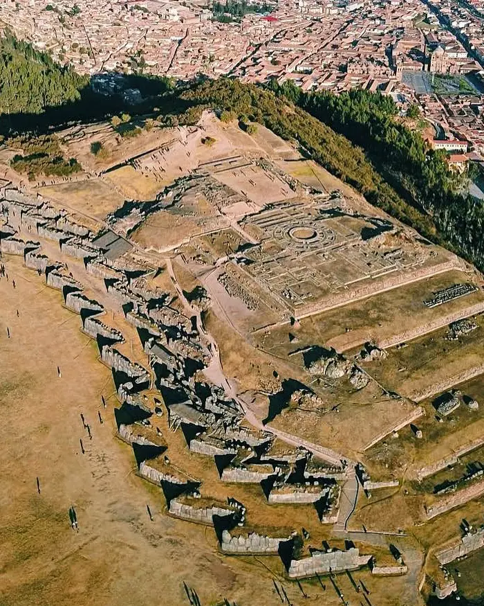 Aerial view of Sacsayhuaman in Cusco, Peru, showing the long zigzag Inca stone walls stretching across a dry hillside under clear skies.