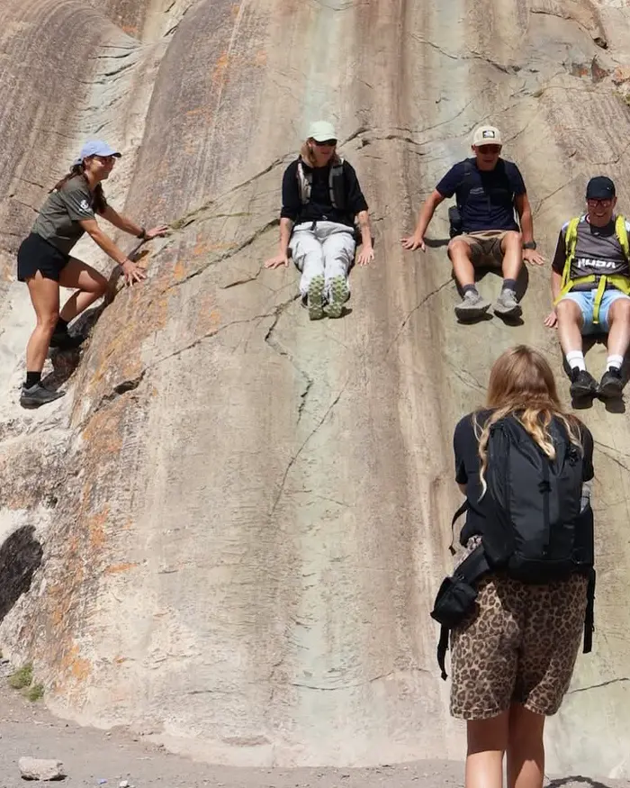 Travelers sitting on smooth rock ledges at the Rodadero in Sacsayhuaman, Cusco, Peru, preparing to slide down with caution.