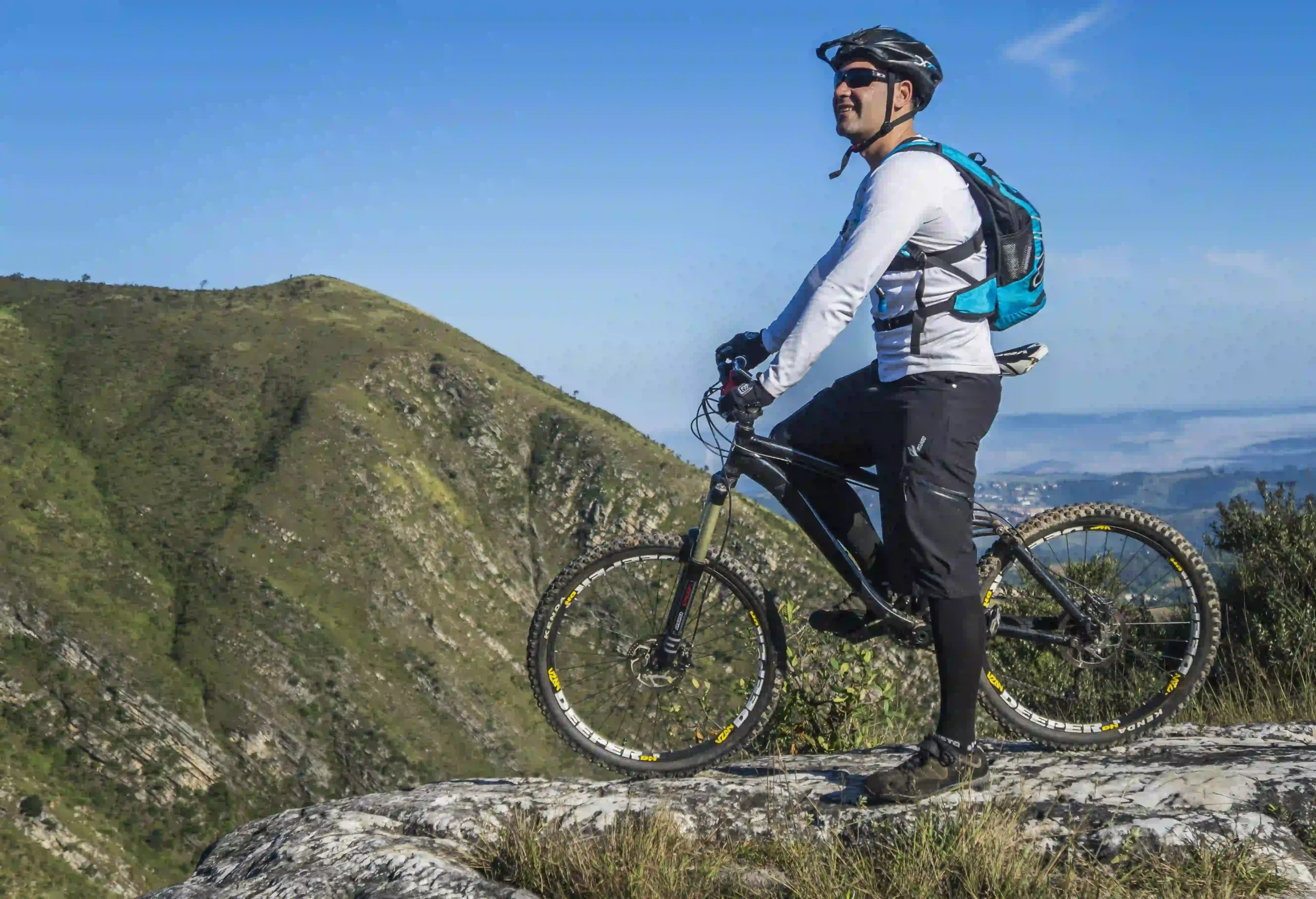 Geared cyclist observing the Sacred Valley mountains from a rocky summit, preparing to ride down escaleras incas en mountain biking in Cusco.