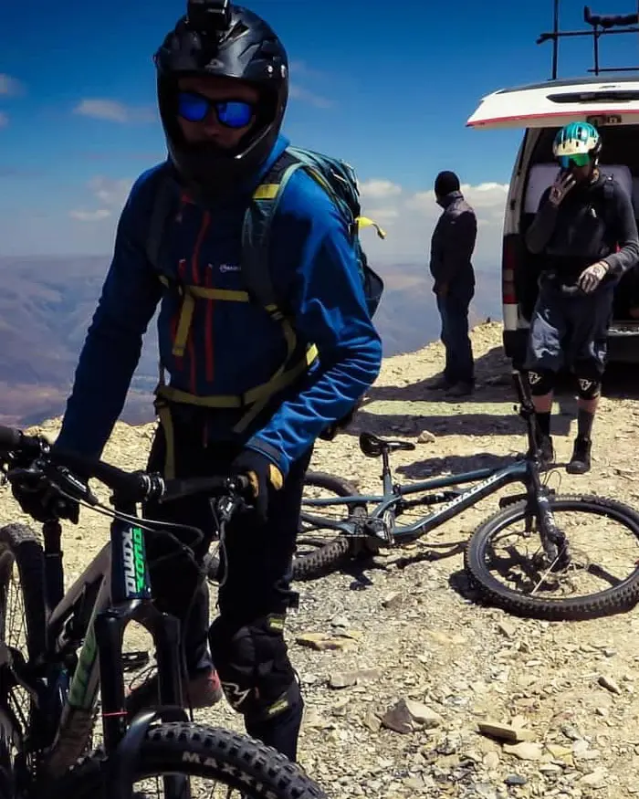 Rider wearing a full face helmet and dark goggles, ready to ride on rocky high mountain terrain.