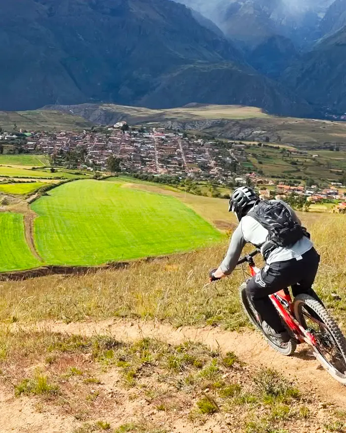 Mountain biker descending a fast dusty trail in Cusco, Peru, above green valleys, with open terrain and wide views.