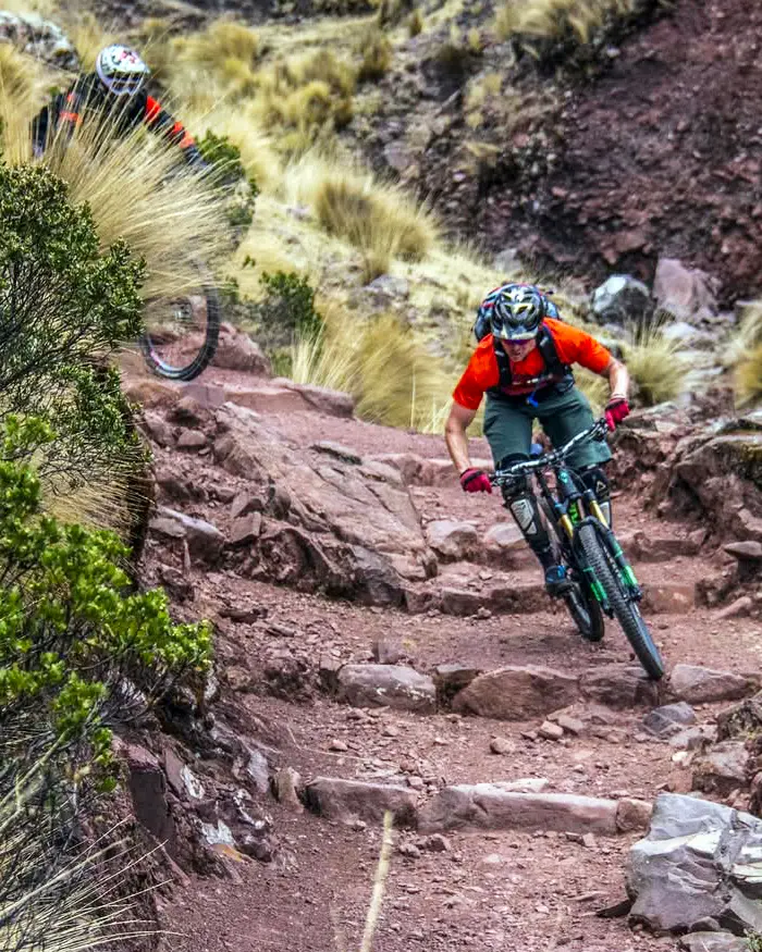 Mountain biker on a technical rocky trail in Cusco, Peru, rolling natural step ups and loose rocks with ichu grass and shrubs along the track.