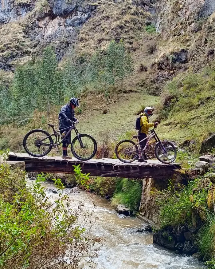 Mountain biker descending a fast dusty trail in Cusco, Peru, above green valleys, with open terrain and wide views.