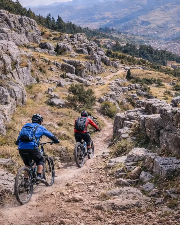 Dos ciclistas descienden por un sendero exterior entre formaciones rocosas y muros de piedra en la zona de Qenqo.