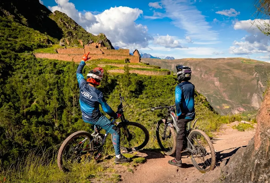 Two mountain bikers in blue gear observe ancient stone ruins from a dirt path while riding Enduro in Cusco on the Perolniyoc trail