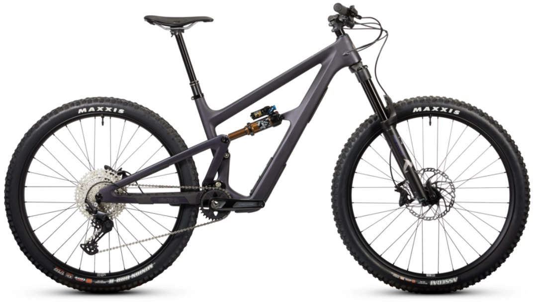 "Product photograph of Ibis Ripmo V3 bicycle in side profile on white background, matte dark gray carbon frame, dual suspension with visible rear shock featuring gold spring, black suspension fork, aggressive Maxxis tires, large disc brakes, wide-range silver cassette, dropper seatpost, modern trail/all-mountain design"