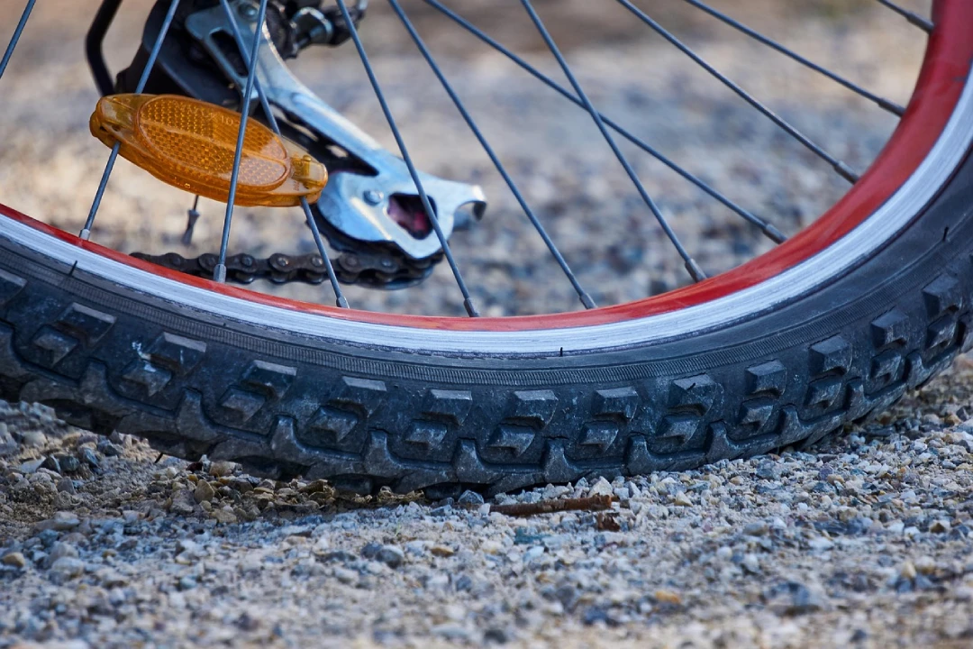 Close-up of a bicycle wheel with a low, flat tire resting on gravel, showing the tread, rim, and spokes.