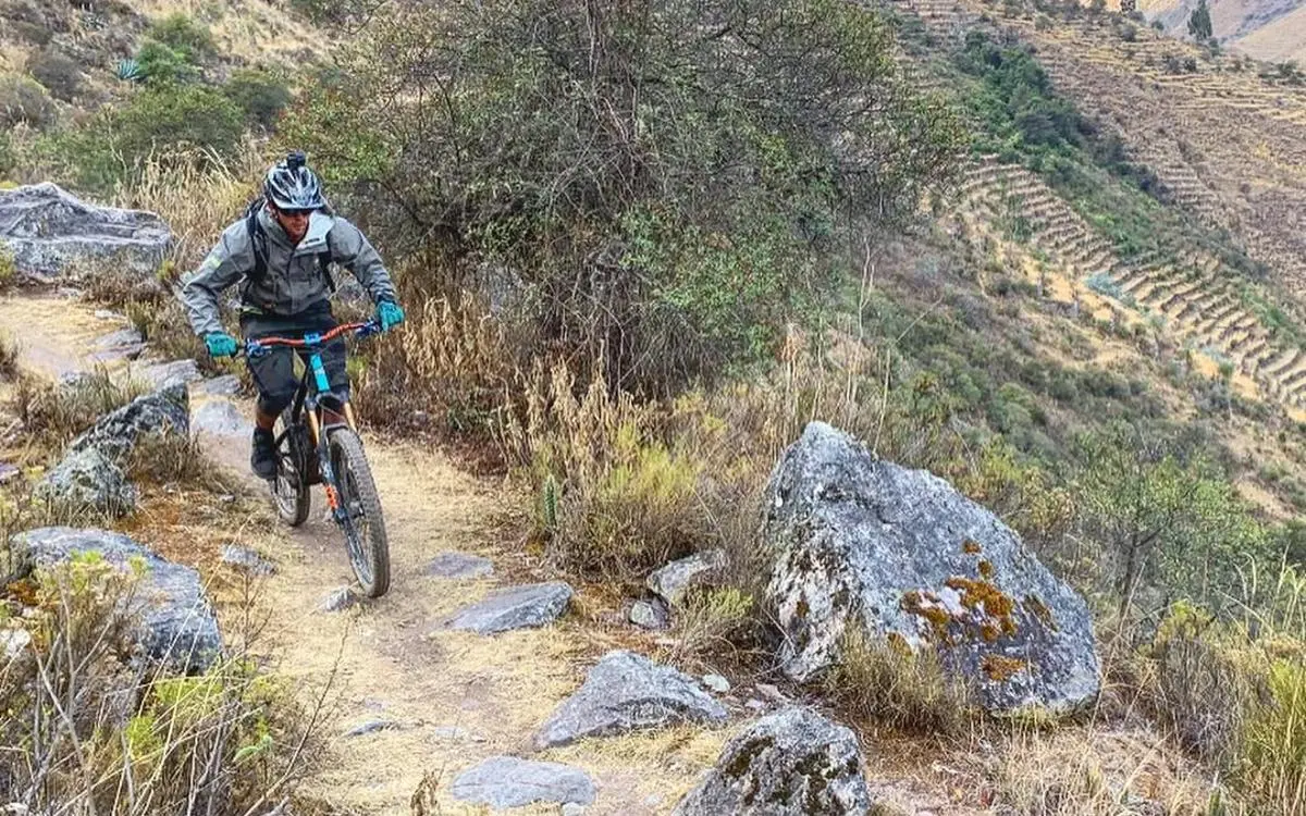 A cyclist descends with control along a narrow trail surrounded by rocks and dry vegetation.