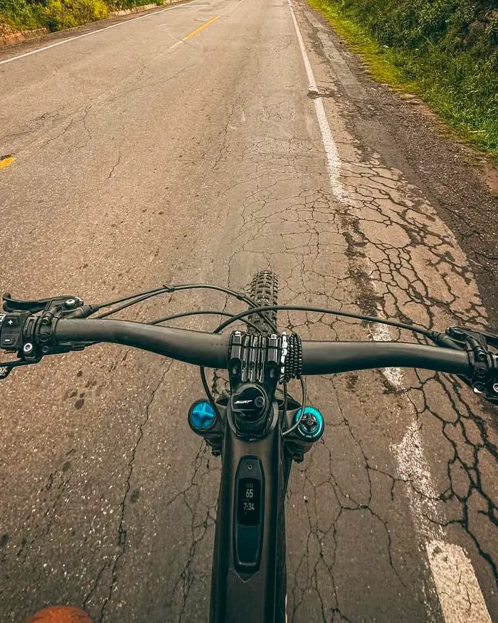 A cyclist riding along a long, open road, surrounded by vegetation on both sides.