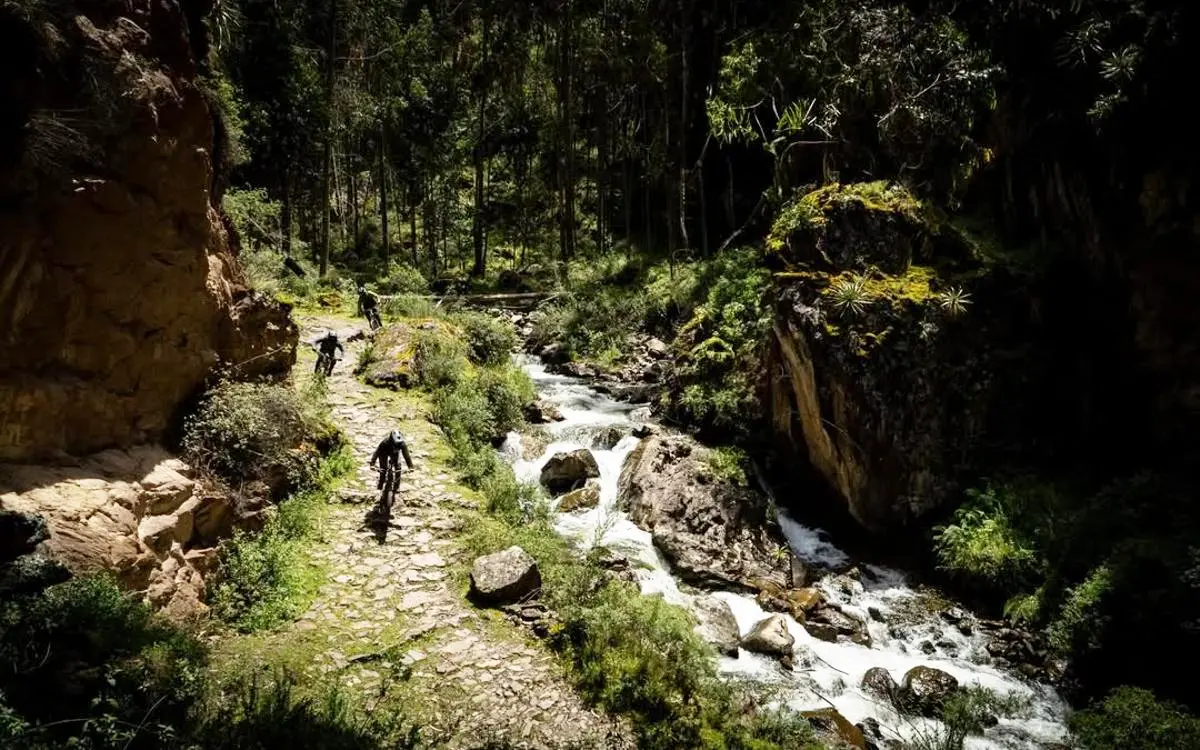 Un grupo de ciclistas recorre un sendero de piedra junto a un río, iniciando uno de los descensos largos hacia el Valle Sagrado.