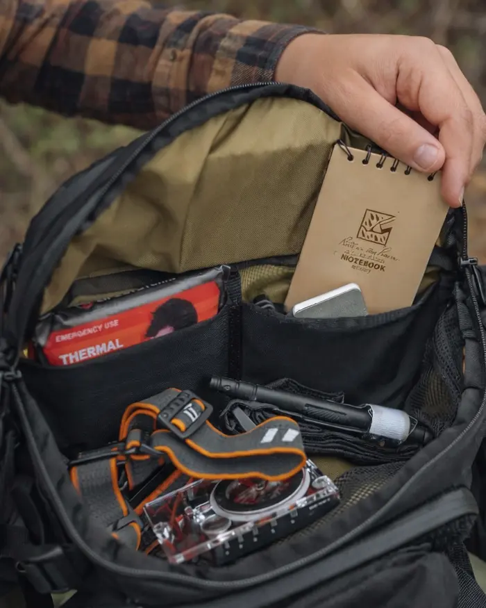 A person opens their hip pack, revealing a well-organized interior with different compartments for essential gear.