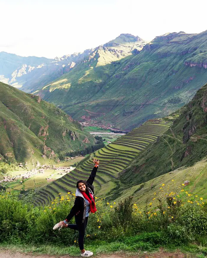 Una viajera posa con entusiasmo frente a un impresionante valle andino lleno de terrazas agrícolas.
