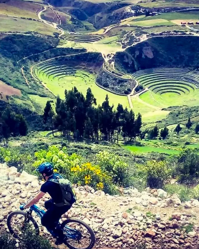 The image shows a rider moving through technical terrain with privileged views of the circular terraces of Moray.