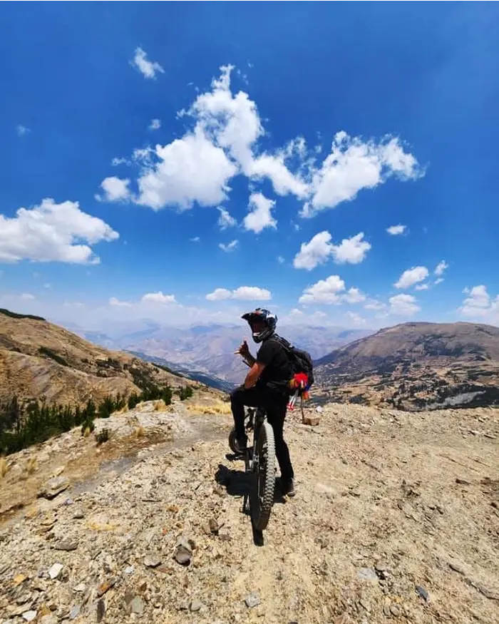The rider keeps his balance next to his bike while looking out over the valley stretching into the distance.