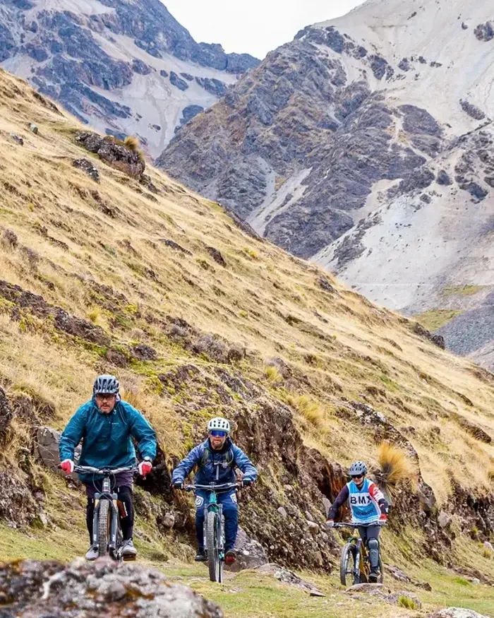 Three mountain bikers ride along a narrow trail in a high mountain area.