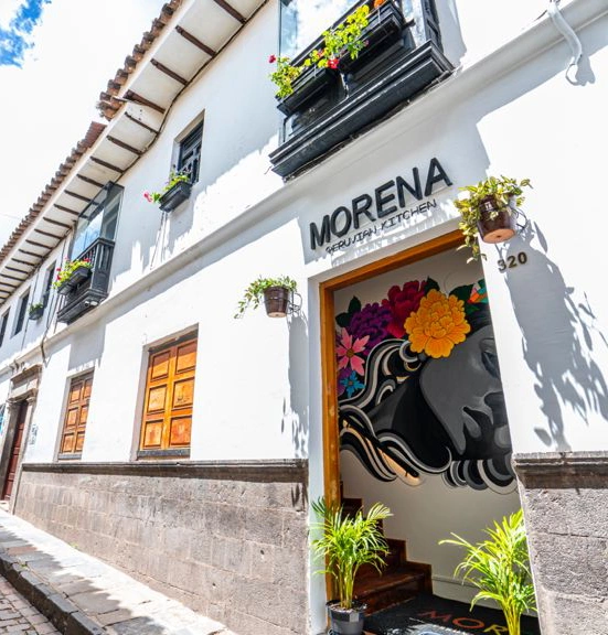 Fachada de Morena Peruvian Kitchen en Cusco, edificio colonial blanco con un mural colorido en la entrada y balcones con flores.